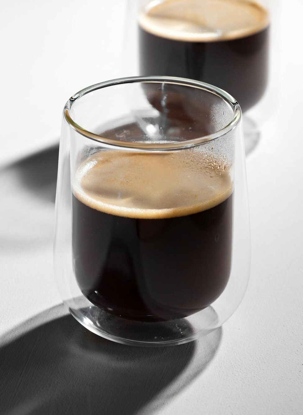 Americano coffee in glass cups on white background with long shadows